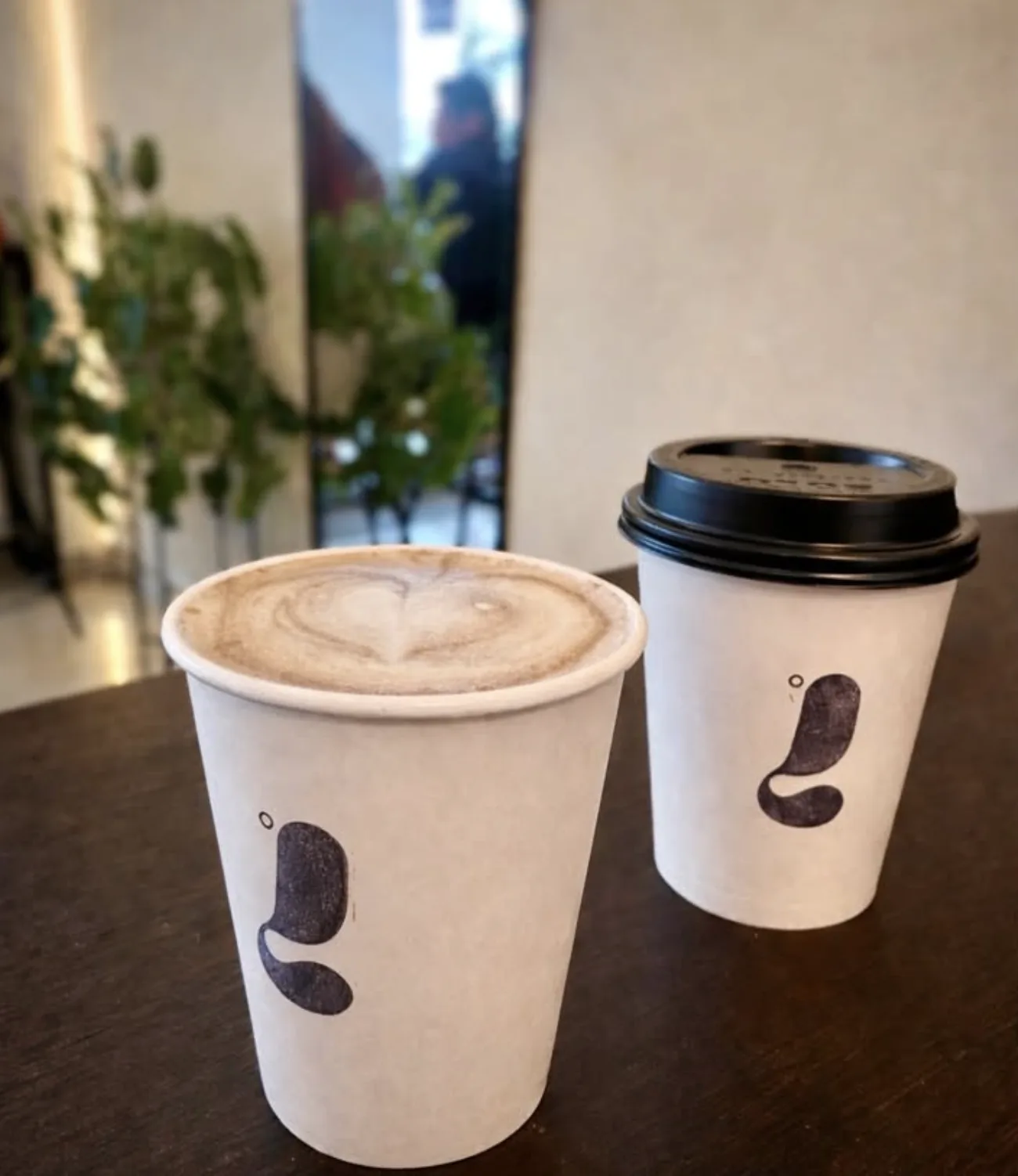 Two LATTITUDE cups on a table, a latte with heart art next to a to-go cup
